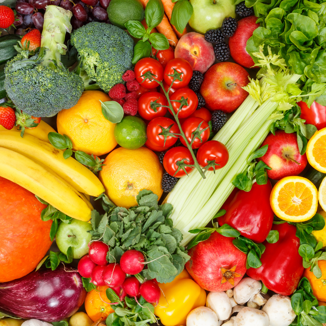A colorful assortment of fresh fruits and vegetables, including bananas, apples, oranges, tomatoes, broccoli, radishes, lettuce, celery, bell peppers, mushrooms, berries, and more, arranged closely together.