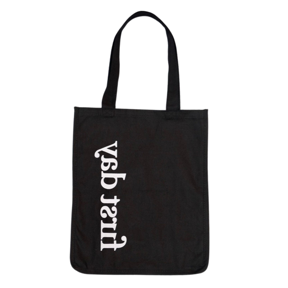 The Reflection Tote features "first day" in white, rotated 90° counterclockwise along the left, with a minimalist black design and two handles for a subtle hidden message.