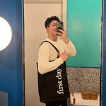 A person takes a mirror selfie in a well-lit bathroom with blue and teal walls, wearing a cream sweater and holding the Reflection Tote, which features 