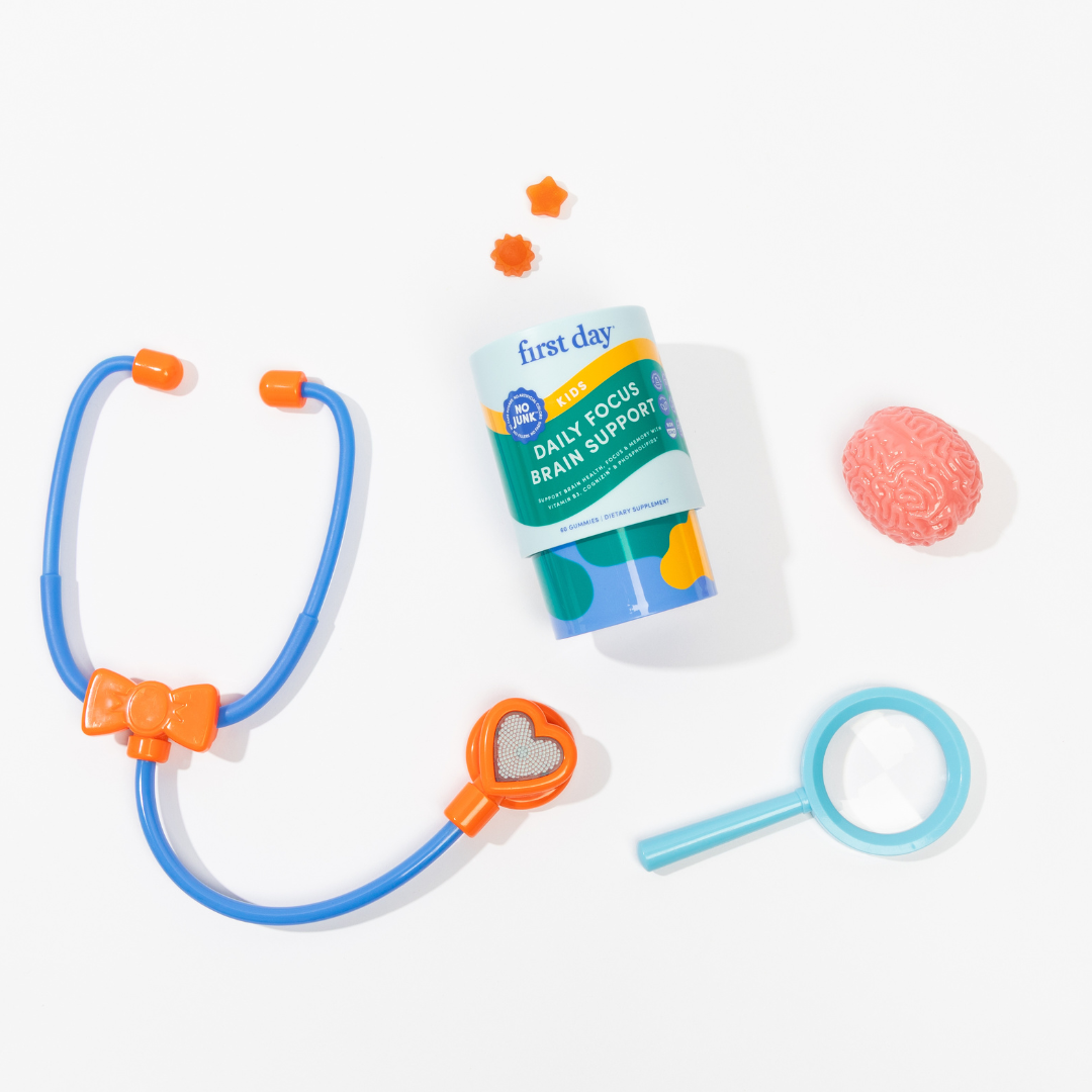 A toy stethoscope, magnifying glass, pink brain model, two orange toy gears, and a container labeled Daily Focus Brain Support are arranged on a white surface.